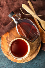 wooden plate with bottle and bowl of tasty maple syrup on table