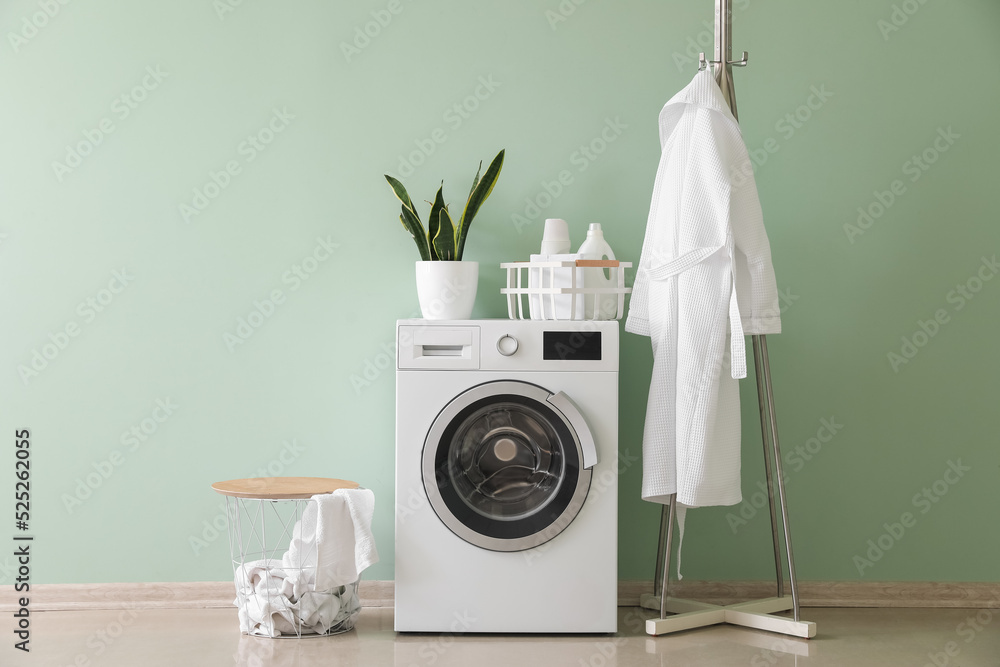 Interior of stylish laundry room with washing machine, rack and bathrobe