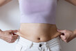Cropped image of overweight woman, tucking, hiding fat naked big excessive belly with navel in white jeans. Dangling down stomach, big size tummy. Drag away of abdomen. Go on diet, liposuction