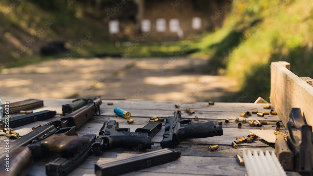 Numerous guns, rifles, and ammunition bullets placed on a wooden table ...