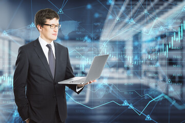 Wall Mural - businessman using laptop with abstract glowing forex chart, map and arrows on index hologram, blurry office interior background. Trade, financial growth, analytics and market concept. Double exposure.