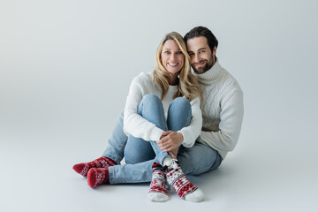 full length of smiling couple in winter outfits and red socks with ornament sitting on grey