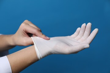 Wall Mural - Doctor putting on medical gloves against blue background, closeup