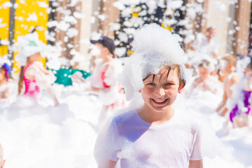 happy little boy with foam on his head, in wet clothes at a foam party or holiday on a sunny hot summer day