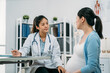 © PR Image Factory - female chinese gynecologist holding a pen is listening attentively while her pregnant patient is telling her about problems at desk in a modern bright clinic.
