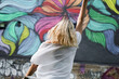 © brillianata - Pretty young woman with blond hair standing on a street with the graffiti wall background. View from the back