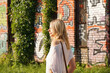 © brillianata - Pretty young woman with blond hair standing on a street with the graffiti wall background. View from the back