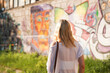 © brillianata - Pretty young woman with blond hair standing on a street with the graffiti wall background. View from the back