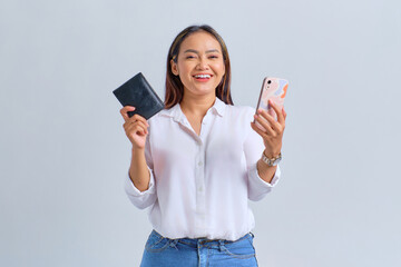 Wall Mural - Cheerful young Asian woman holding mobile phone and wallet isolated over white background