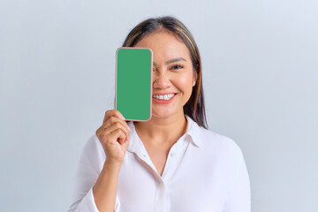 Wall Mural - Smiling young Asian woman covering half face with blank screen mobile phone, recommending mobile app isolated over white background