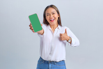 Wall Mural - Cheerful young Asian woman showing mobile phone blank screen and showing thumb up gesture isolated over white background