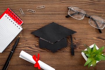 Black academic cap or graduation hat on students table, top view