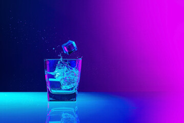 Wall Mural - Ice cube falls into a transparent glass of water standing on mirror surface over gradient blue-pink background in neon light. Art, beauty, drinks