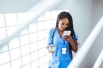 Portrait of young woman doctor in  scrubs sitting while using smartphone in hospital, relax after working day. Nurse Using Her Mobile Phone While Taking a Break.