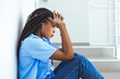 © Dragana Gordic - Shot of a young female nurse looking stressed out while seating at a window in a hospital. Tired female nurse in hospital corridor. Female nurse suffering from headache.