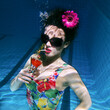 beautiful woman in a colourful stylish swimsuit and sunglasses and pink gerbera in the head with a cocktail  in her hand underwater in the swimming pool