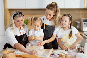 Surprised little daughter holding homemade dough in arms examining. Eldelry granny taking flour for sprinkling. Young mother holding large bowl. Older daughter talking looking at father.