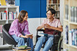 © Seventyfour - Portrait of smiling young man in wheelchair talking to friend while studying together in library