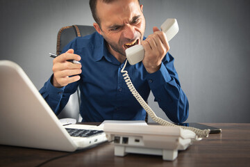 Wall Mural - Caucasian angry businessman screams into the telephone receiver.