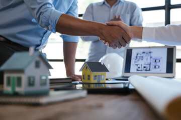 Close up of handshaking of engineer and architect after on paperworks and floor plan drawings about design and building houses.