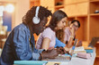 © Seventyfour - Diverse group of students in row using laptops and studying in college library, focus on black young man wearing headphones in foreground