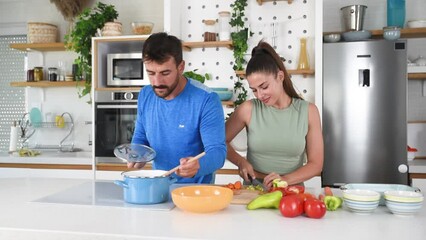 Wall Mural - Young sporty man and woman couple cutting and together cooking fresh natural vegetables at kitchen and cooking for healthy lunch. Self care yoga nutritionists having healthy meal after home workout.