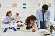 © Seventyfour - Portrait of young male teacher helping African American girl in school classroom, copy space