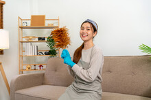 Housekeeper Is Wearing Protective Gloves And Holding Feather Duster To Cleanups And Dusting In Living