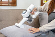 Housekeeper is using cordless vacuum cleaner with handheld for cleanups and vacuuming dirt on furniture