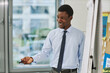 © Seventyfour - Side view portrait of smiling black teacher standing by whiteboard and talking to class