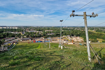 Wall Mural - Downhill ski track with lifts without snow in summer day and view of Ventspils city, Latvia.