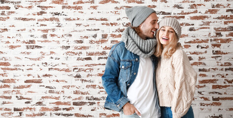 Wall Mural - Happy young couple in warm autumn clothes near brick wall with space for text