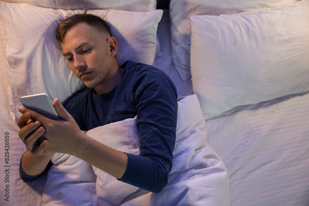 Young man using mobile phone in bedroom at night