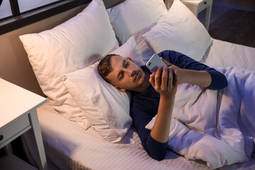 Wall Mural - Young man using mobile phone in bedroom at night