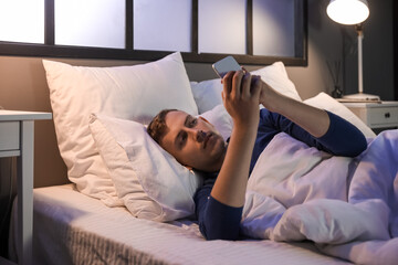 Canvas Print - Young man using mobile phone in bedroom at night