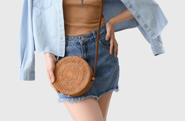 Young fashionable woman with rattan handbag on light background