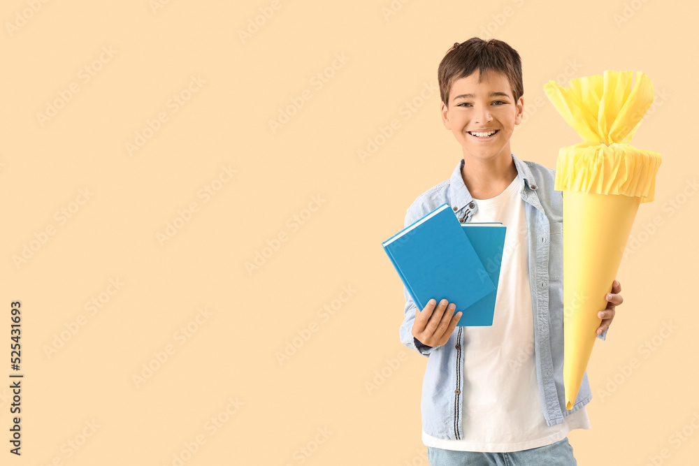 Little boy with yellow school cone and books on beige background