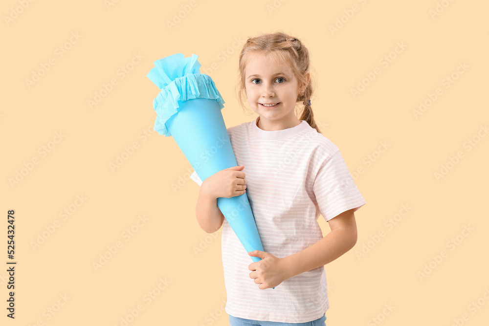 Cute little girl with blue school cone on beige background