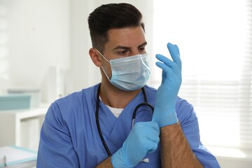 Canvas Print - Doctor in protective mask putting on medical gloves indoors