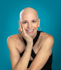 Confident mature over 50 woman survivor with alopecia sitting hand to chin isolated on blue background