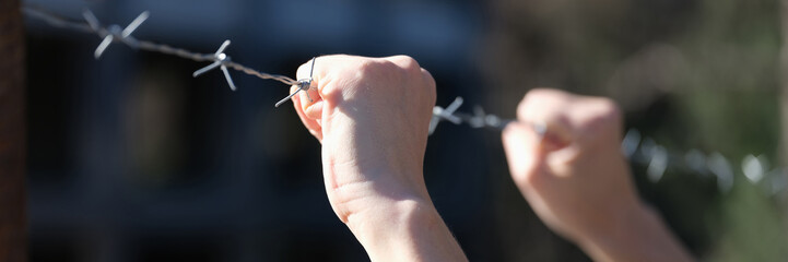 Woman holding hands on barbed wire closeup