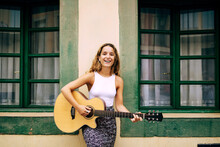 Curly Woman Playing Guitar Leaning On The Wall