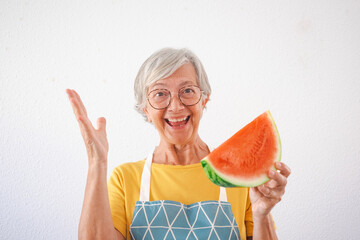 Wall Mural - Cheerful attractive old senior woman holding a slice of fresh watermelon looking at camera isolated on white background - healthy eating lifestyle concept