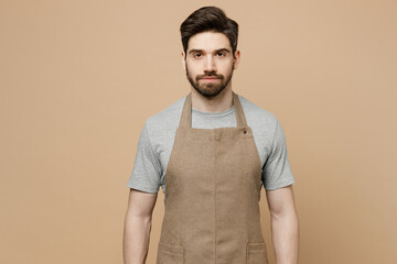 Young confident caucasian man barista barman employee in brown apron work in coffee shop looking camera isolated on plain pastel light beige background studio portrait Small business startup concept