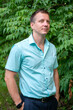 © Beliakina Ekaterina - Portrait of a 30-40-year-old man in a light green shirt against a green tree in summer