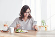 © amanaimages - スマホを見ながら食事をする若い日本人女性