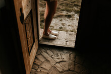 A Woman Is Standing Outside The Threshold Of A Door. Rustic Vintage Stone Brick Pavement Inside And Outside. Beautiful Hand Carved Door. Dark Copy Space. 