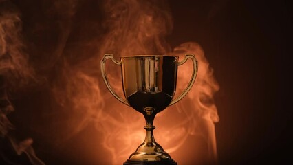 Wall Mural - the golden trophy on a black background smokes around a fierce and fiery concept of competition or v