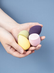 Woman holds group of soft sponges for makeup on blue background