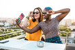 © ADDICTIVE STOCK - Happy lesbian couple taking selfie on balcony
